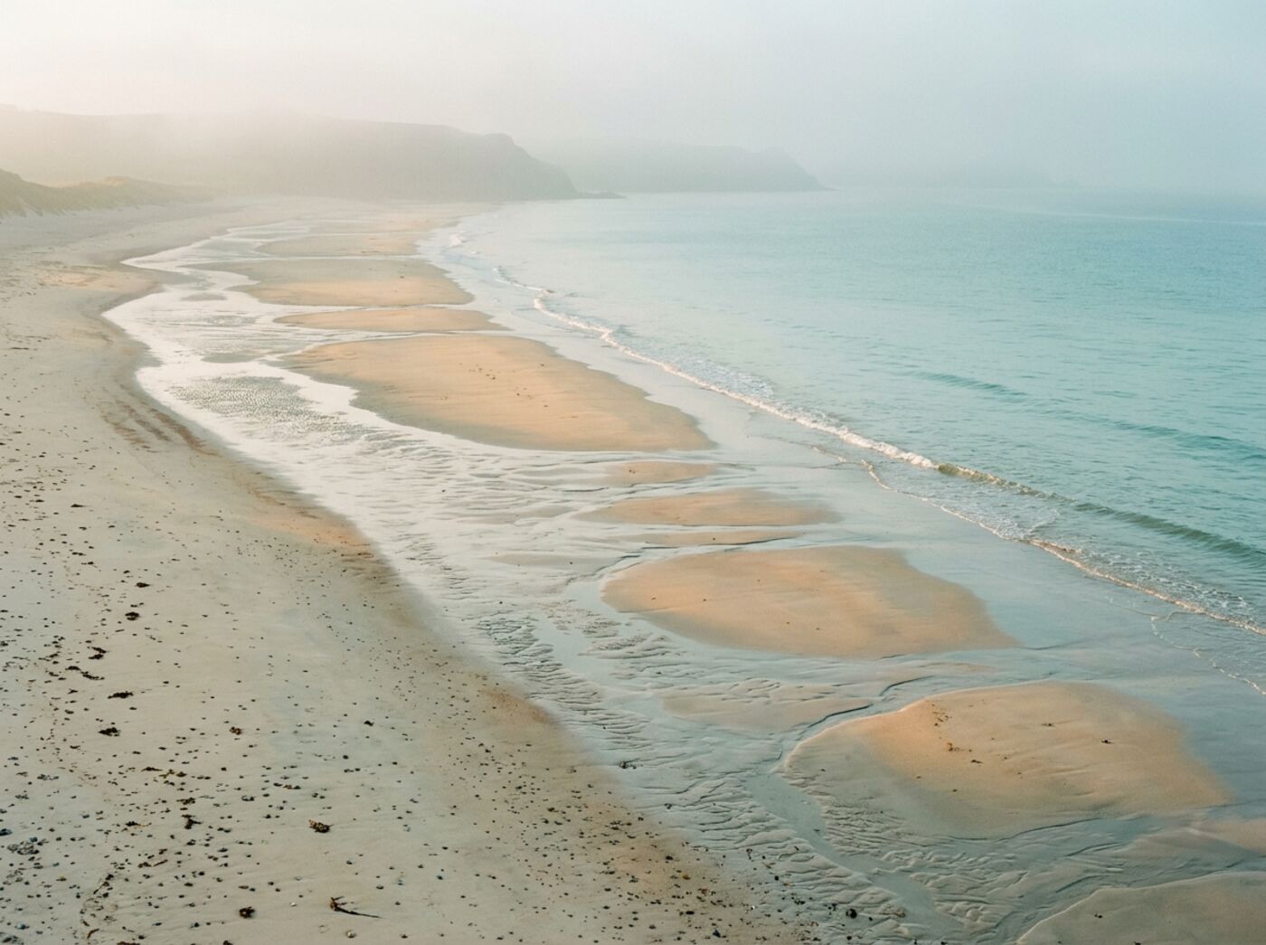 Misty coastline at dawn with gentle tide lines on pale sand