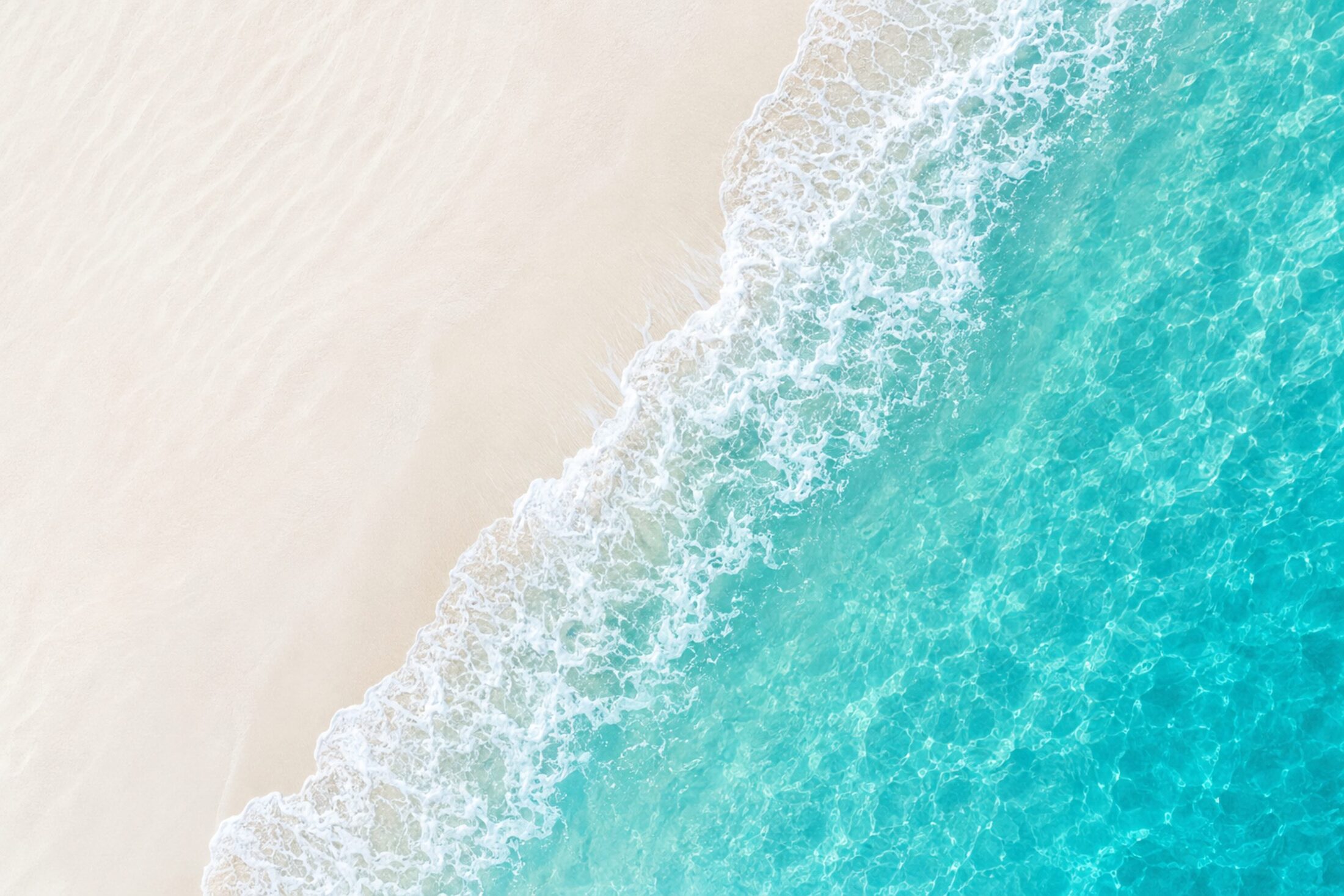 Aerial view of a turquoise wave washing onto pale sand